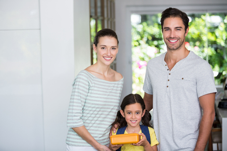 Portrait of smiling family with daughter holding lunch box at homeの写真素材