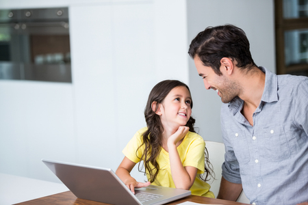 Smiling daughter using laptop with father at homeの写真素材