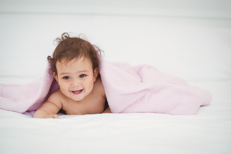 Cute smiling baby lying under blanket at homeの写真素材