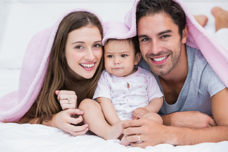 Portrait of smiling couple with baby on bed at home