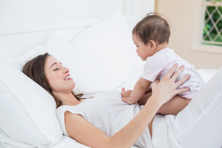 Young woman playing with daughter while lying on bed at homeの写真素材