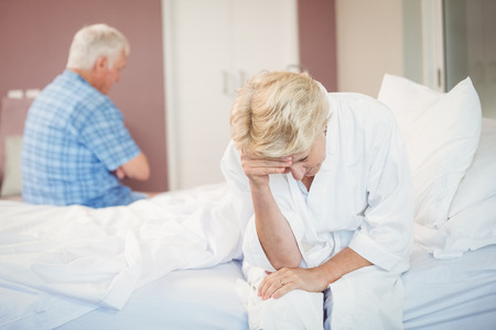 Tensed senior couple sitting in bedroom at homeの写真素材