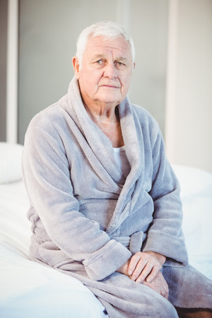 Portrait of suffering senior man sitting on bed at homeの写真素材