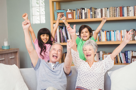 Grandparents with grandchildren gesturing success sign at homeの写真素材