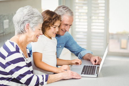 Happy girl with grandparents using laptop at homeの写真素材
