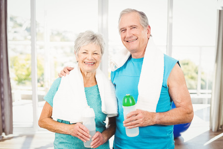 Portrait of happy senior couple holding bottle while exercising at homeの写真素材