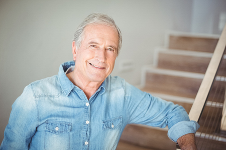 Portrait of smiling senior man against staircase at home