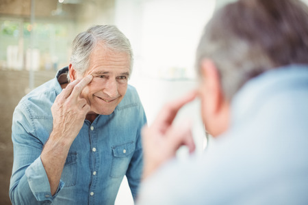 Reflection of senior man looking at skin in mirror in bathroomの写真素材