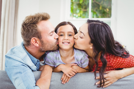 Mother and father kissing daughter while leaning on sofa at homeの写真素材