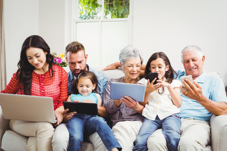 Happy family using technologies while sitting on sofa at homeの写真素材