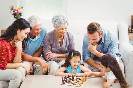 Parents and grandparents looking at girls playing chess at homeの写真素材