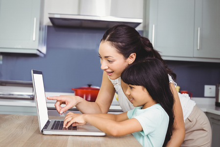 Happy mother and daughter working on laptop at homeの写真素材