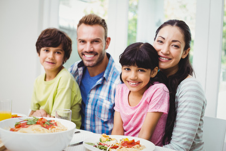 Portrait of smiling parents and siblings at dining table in homeの写真素材