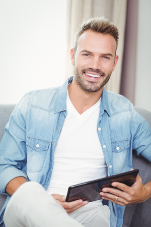 Portrait of smiling young man holding digital tablet at homeの写真素材