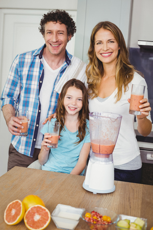 Portrait of smiling family with fruit juice in kitchenの写真素材