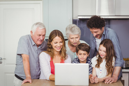 Family looking into laptop on table in kitchen at homeの写真素材