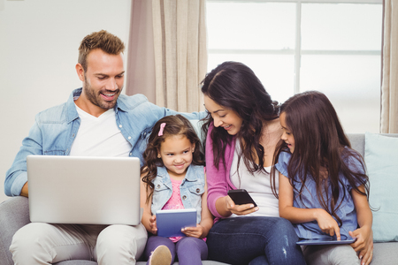 Family using modern technologies while sitting on sofa at homeの写真素材