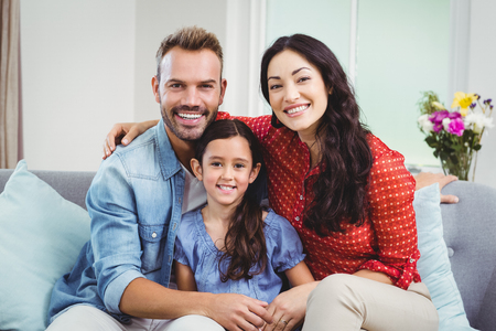 Portrait of happy parents sitting with daughter on sofa at homeの写真素材