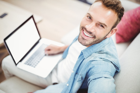 High angle portrait of happy man using laptop on sofa at homeの写真素材