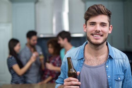 Portrait of smiling young man holding beer bottle while friends enjoying in backgroundの写真素材