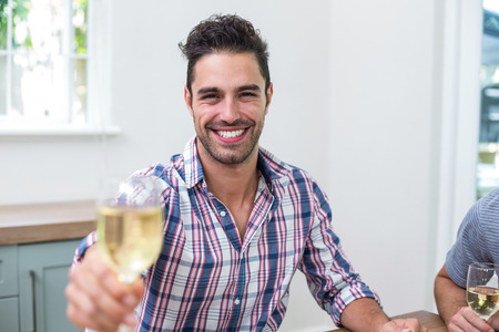 Portrait of handsome young man showing wineglass while sitting in houseの写真素材