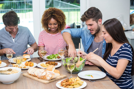 Happy young friends having meal at table in houseの写真素材