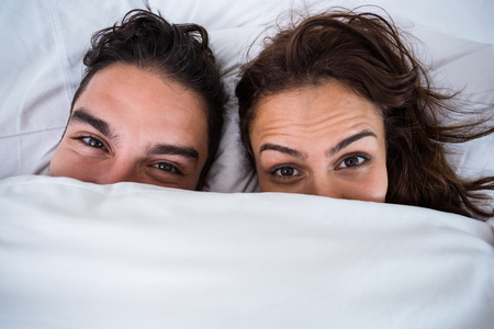 Close-up portrait of couple relaxing on bed at homeの写真素材