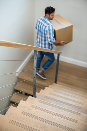 High angle view of man holding cardboard box while walking on stairway of houseの写真素材