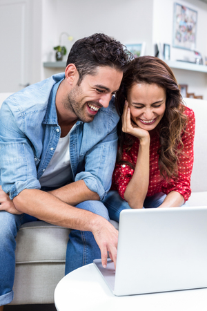 Cheerful couple using laptop at homeの写真素材