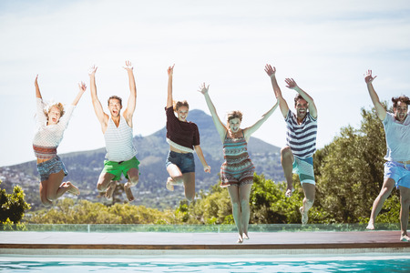 Group of friends jumping in swimming pool with their hands raisedの写真素材
