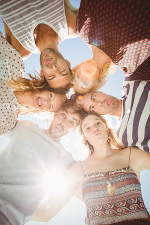 Group of happy friends making funny faces while forming a huddle against skyの写真素材