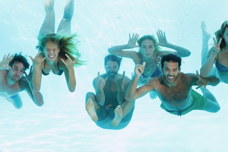 Group of young friends having fun underwater in swimming poolの写真素材