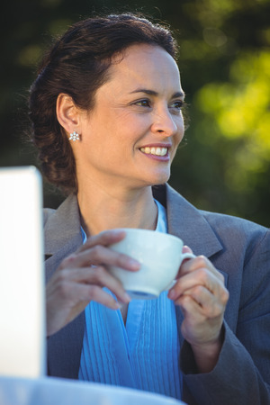 Smiling businesswoman drinking coffee with laptop in a restaurantの写真素材