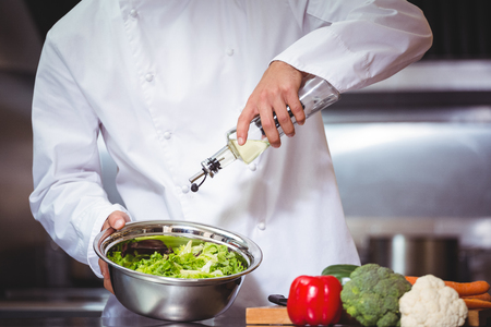 Chef putting oil on salad in commercial kitchenの写真素材