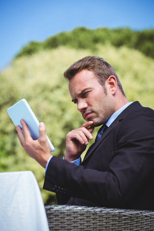 Thoughtful businessman using tablet sitting outside a restaurantの写真素材