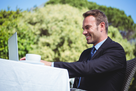 Businessman using laptop and having a coffee sitting outside a restaurantの写真素材