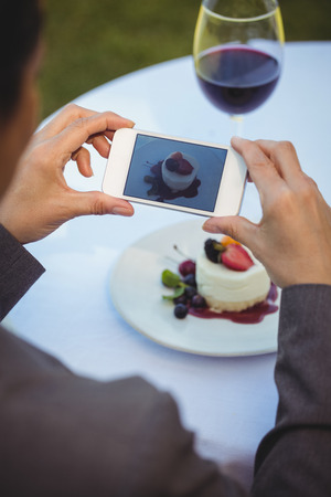 Woman taking a photo of her dessert in a restaurantの写真素材