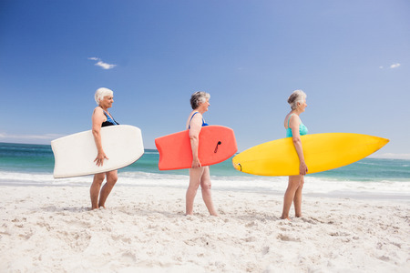 Senior woman friends holding surfboard on the beachの写真素材