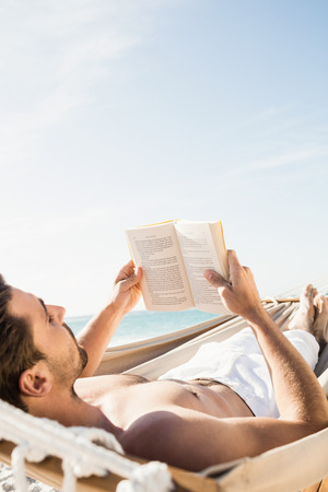 Man reading book in hammock on the beachの写真素材