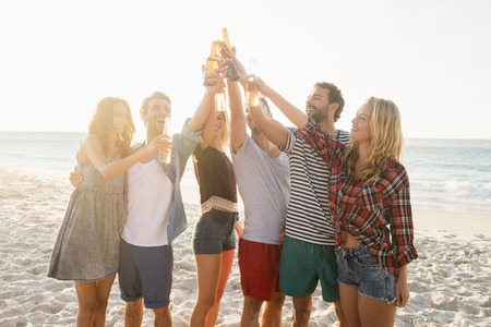 Happy friends raising beer bottles on the beachの写真素材