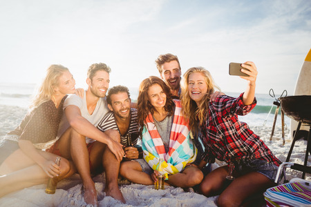 Happy friends taking selfie with smartphone on the beachの写真素材