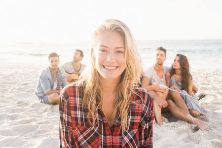 Smiling friends sitting on sand on the beachの写真素材