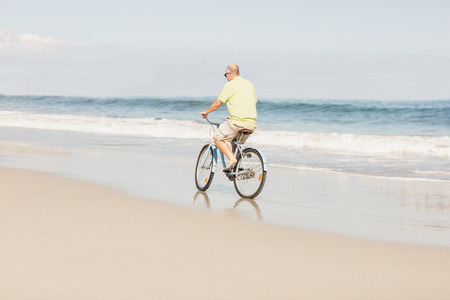 Smiling senior man riding bike on the beachの写真素材