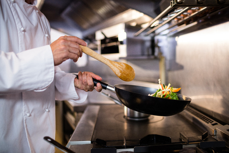 Mid section of chef preparing food in the kitchen of a restaurantの写真素材