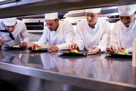 Team of chefs garnishing dishes on commercial kitchen counterの写真素材