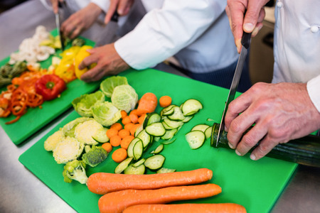 Close-up of chefs chopping vegetables on chopping board in the kitchenの写真素材