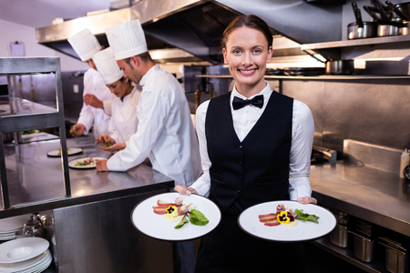 Waitress showing dishes to the camera and team of chefs working in backgroundの写真素材