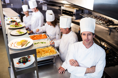Portrait of chef in commercial kitchen and four chef serving at order stationの写真素材