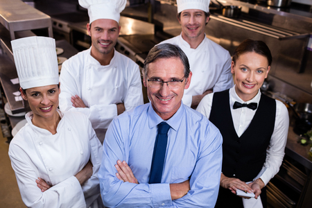 Portrait of happy restaurant team standing together with arms crossed in commercial kitchenの写真素材