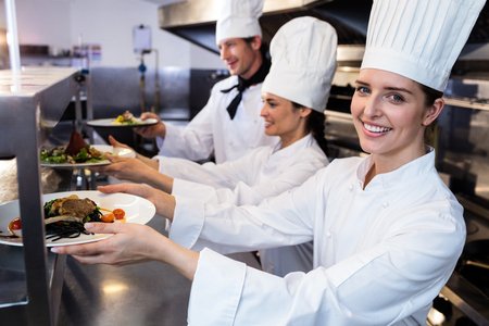 Chefs handing dinner plates through order station in the kitchenの写真素材
